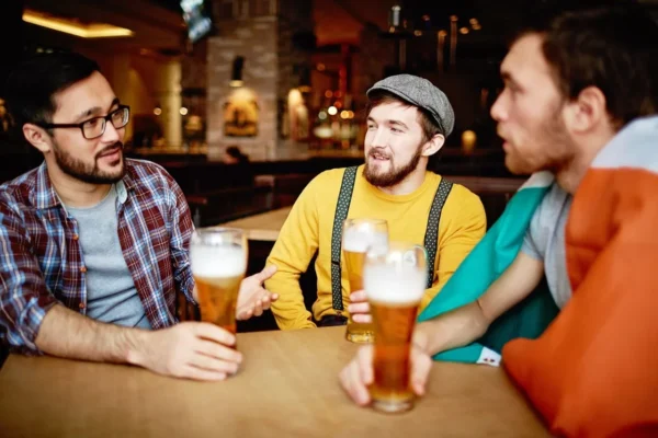 A group of young adults enjoying beers and conversation in a cozy pub setting.